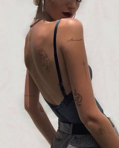 a woman with tattoos on her back standing in front of a white wall and looking off to the side