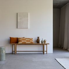 a wooden bench sitting in front of a white wall with two vases on it