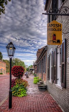 a brick sidewalk with a lamp post and sign on the side that says amish peddler