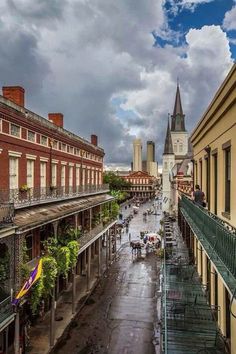 an empty city street with people walking on the sidewalk and buildings in the background under a cloudy sky