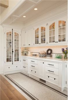 a large kitchen with white cabinets and wood flooring on the side walk leading to an open dining room