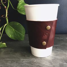 a white and brown coffee cup sitting on top of a table next to a green plant