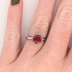 a close up of a person's hand wearing a ring with a red stone