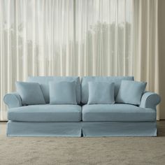 a light blue couch sitting in front of a window with curtains on the windowsill