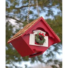 a red birdhouse hanging from a chain with a wreath on it's side