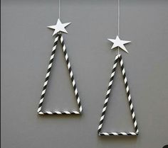 two black and white paper straw christmas trees hanging from strings on a gray wall with stars