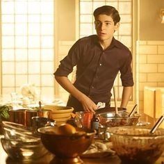 a young man standing in front of a table full of food and bowls with utensils on it