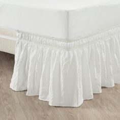 a white bed skirt with ruffles on the bottom and bottom, in front of a wooden floor