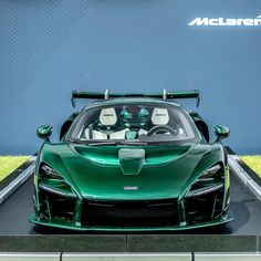 a green sports car is on display in front of a blue wall and grassy area