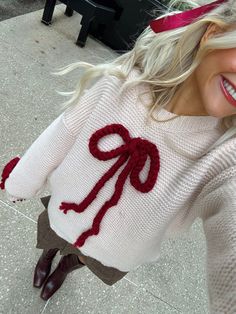 a woman is smiling while wearing a sweater with a bow on it