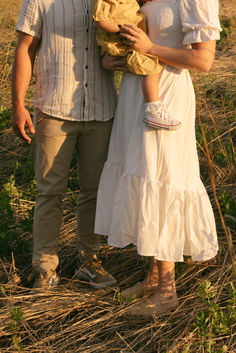 a man and woman holding a baby standing in the middle of a grass covered field