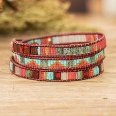 three bracelets with different colored beads on top of a wooden table next to a potted plant