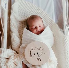 a newborn baby wrapped in a blanket and holding a wooden sign