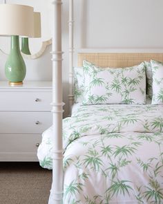 a bed with green palm leaves on it in a bedroom next to a white dresser