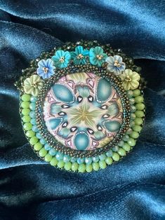 a close up of a brooch with beads and flowers on blue fabric, in the shape of a circle