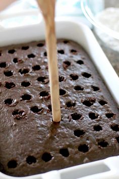 a brownie in a white baking dish with a wooden spoon sticking out of it