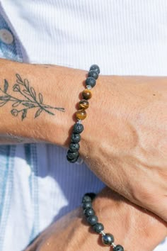 a man with a tattoo on his arm wearing a bracelet made out of lava stone beads