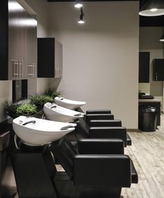 there are many sinks in the room with black chairs