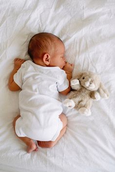 a baby laying on top of a white bed next to a stuffed animal rabbit toy