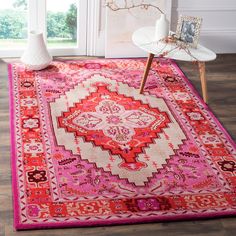 a pink and red rug on the floor in front of a window with white vases