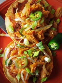 two tacos with meat, onions and green peppers on a red plate next to a fork