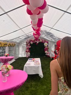 a woman sitting at a table with pink and white balloons hanging from it's ceiling