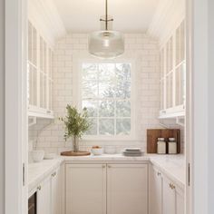 an open door leading to a kitchen with white cabinets and counter tops, along with a potted plant on the window sill