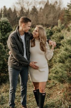 a man and woman standing next to each other in front of christmas tree farm trees