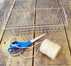 yarn, scissors and twine are sitting on the floor next to a wire basket