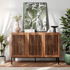 a wooden cabinet sitting next to two potted plants and a painting on the wall