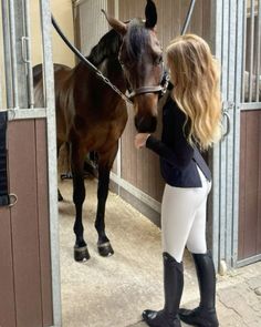 a woman standing next to a brown horse in a stall with her hand on the bridle