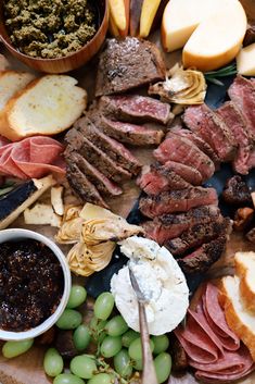 an assortment of meats and cheeses on a platter with grapes, bread