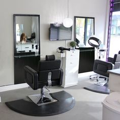 a hair salon with chairs and mirrors in front of the window, one chair is black