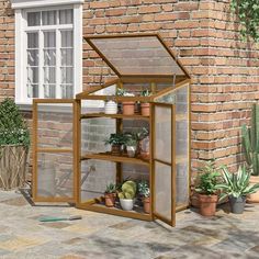 a small greenhouse with plants in it sitting on the ground next to a brick wall