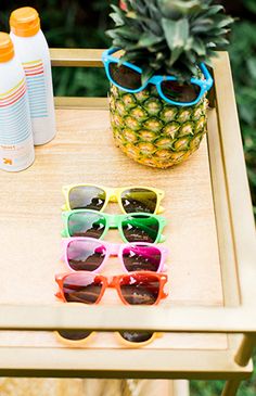 pineapple, sunglasses and sunscreen on a small wooden table with an orange bottle