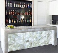 a marble bar in the middle of a kitchen with bottles on the wall behind it