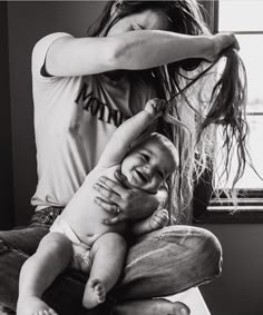 a woman combs her baby's hair while she sits on the floor in front of a window