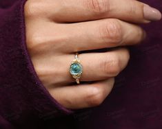 a woman's hand wearing a ring with an oval blue topazte surrounded by diamonds