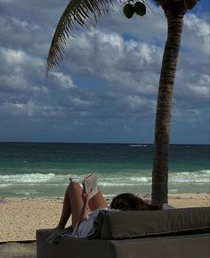 a woman reading a book under a palm tree on the beach