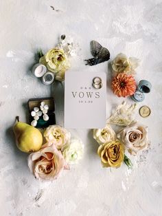 an arrangement of flowers and rings on a white surface with the word vows written in it