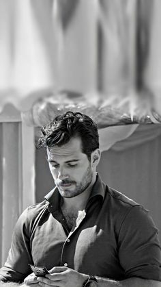 black and white photograph of a man looking at his cell phone while sitting on a bench