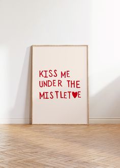 a white framed poster with the words kiss me under the mistlete on it