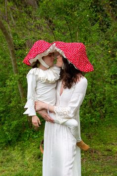 two women in white dresses and red polka dot hats, one holding the other's head