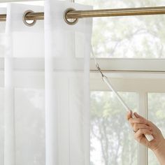 a woman is opening the curtain with her hand and pulling it up from the window