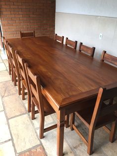 a wooden table with six chairs around it on a tile floor in front of a brick wall