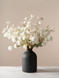 a black vase filled with white flowers on top of a table