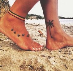 a woman's foot with birds on it and a tree in the sand behind her