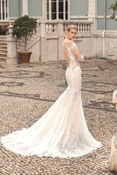 a woman in a wedding dress is standing on a cobblestone street with her back to the camera