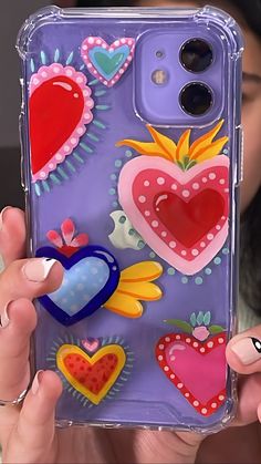 a woman holding up a phone case with hearts and flowers painted on the back of it