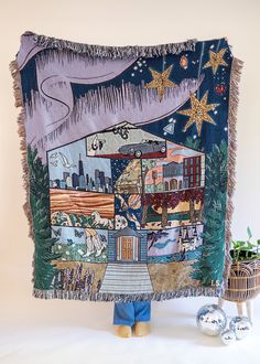 a person holding up a tapestry with buildings and stars in the night sky on it